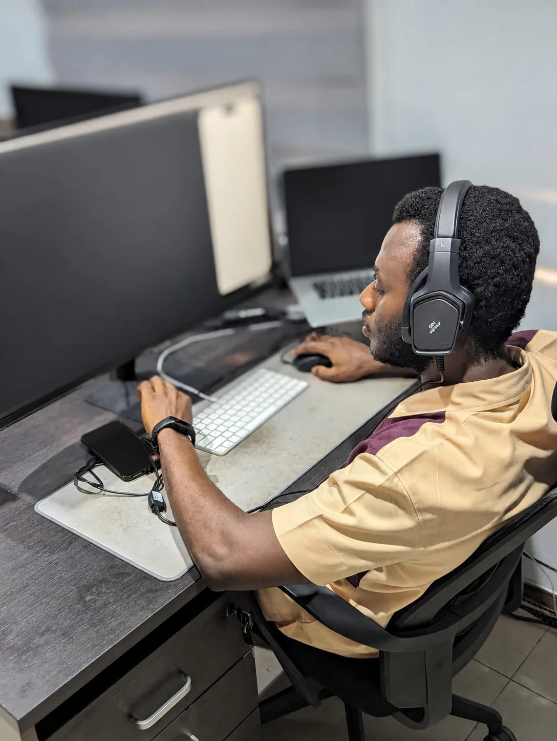 Dacosta Agyei working at a desk with softly blurred computer screens.